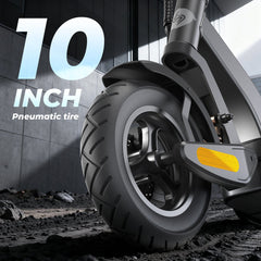 A close-up of a 10-inch pneumatic tire on an electric scooter, featuring a sleek black tread and a reflective yellow strip. The scooter is positioned on a textured, rocky surface with a modern building in the background.